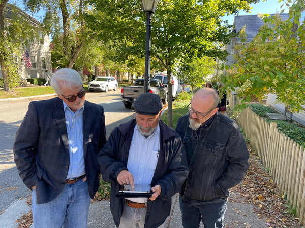 Three men standing on a street, looking at a tablet together.